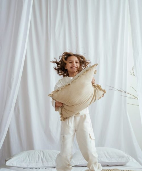 Playing with pillow on the bed. Cute little girl is at home.
